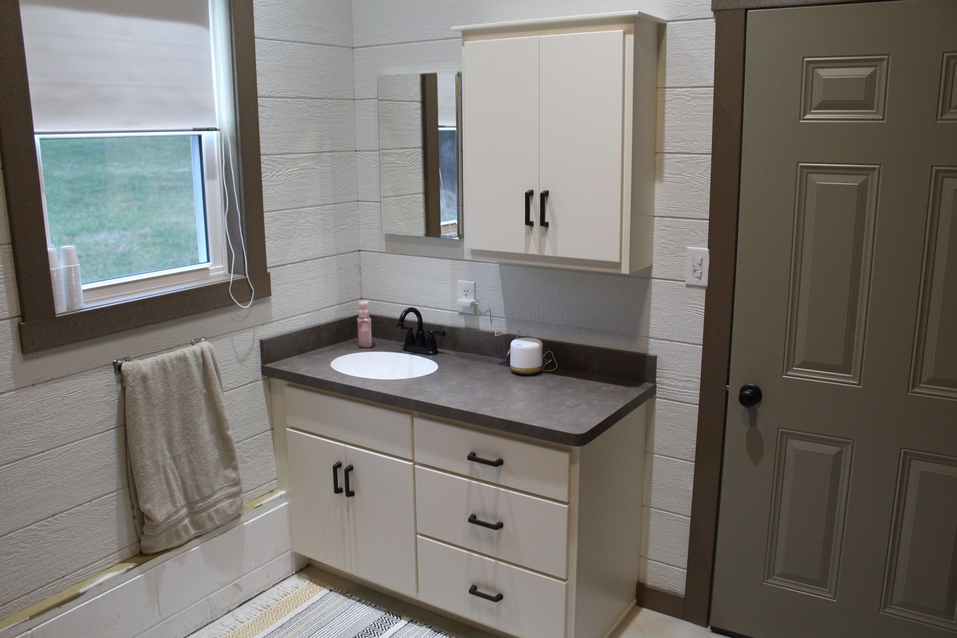 Bathroom with white vanity, sink, cabinet, and window. Beige door and towel.