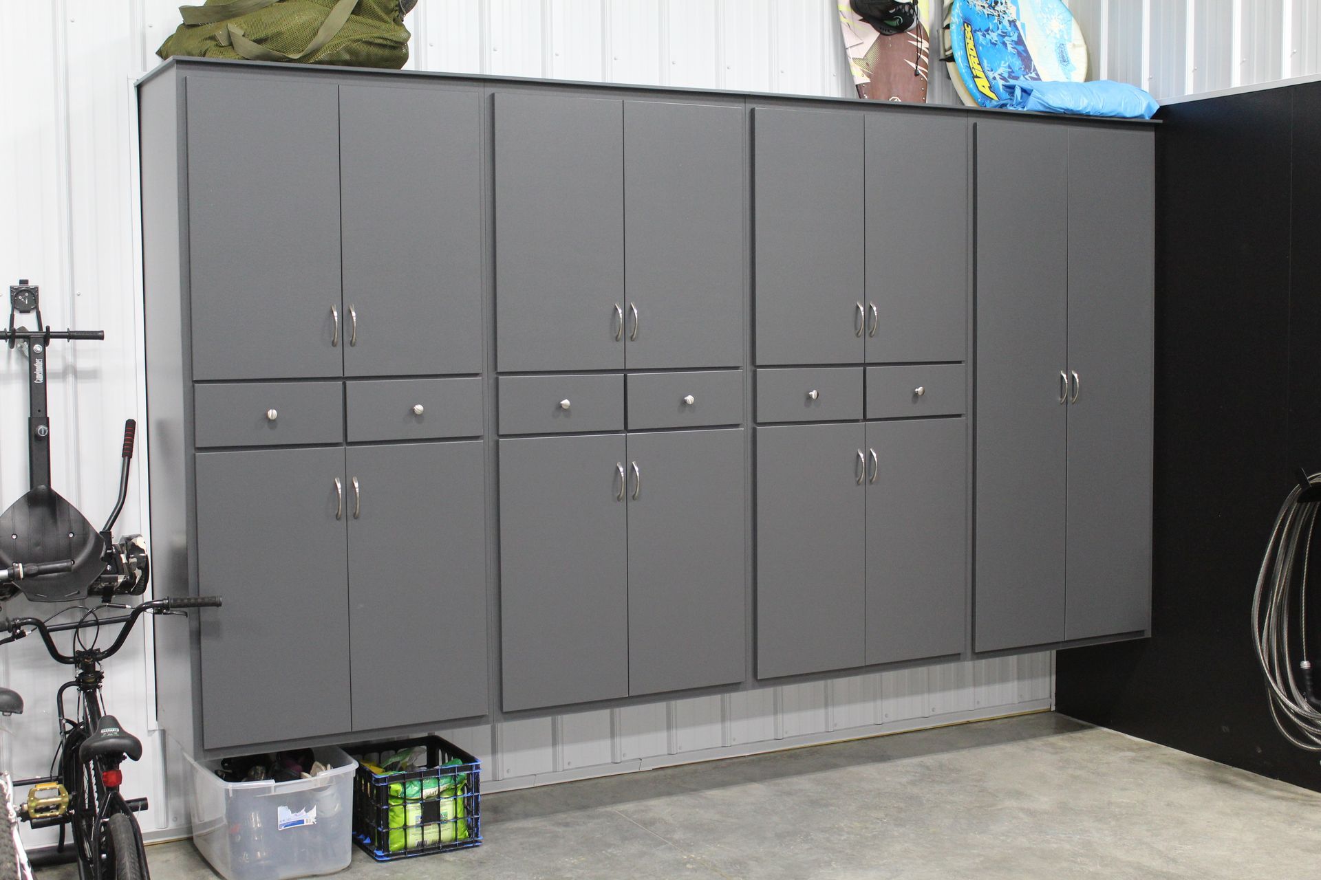 Gray storage cabinets mounted on a white wall in a garage, with various items on top and below.