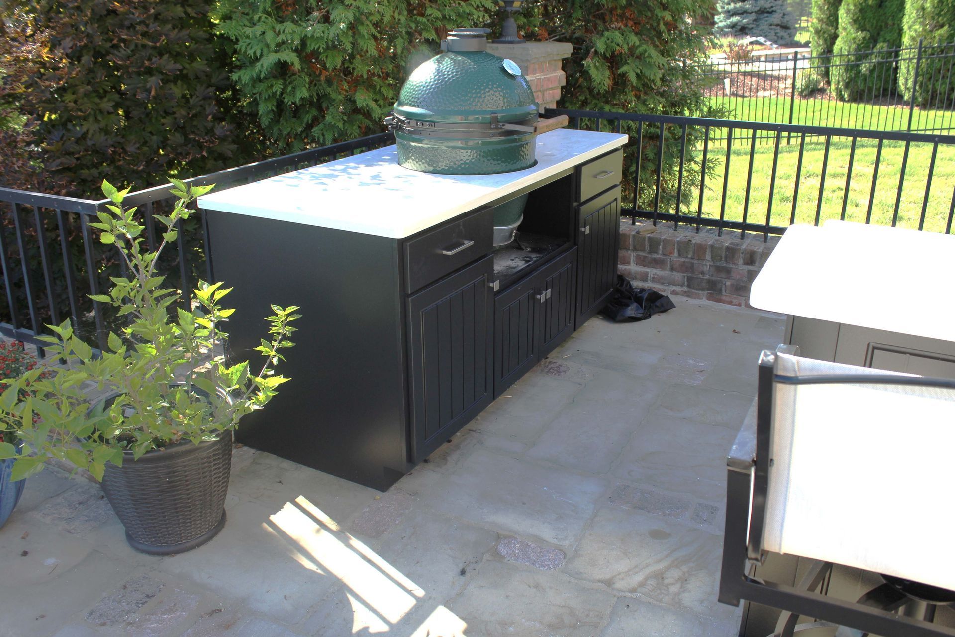 Black outdoor kitchen cabinet with a green grill on a patio.