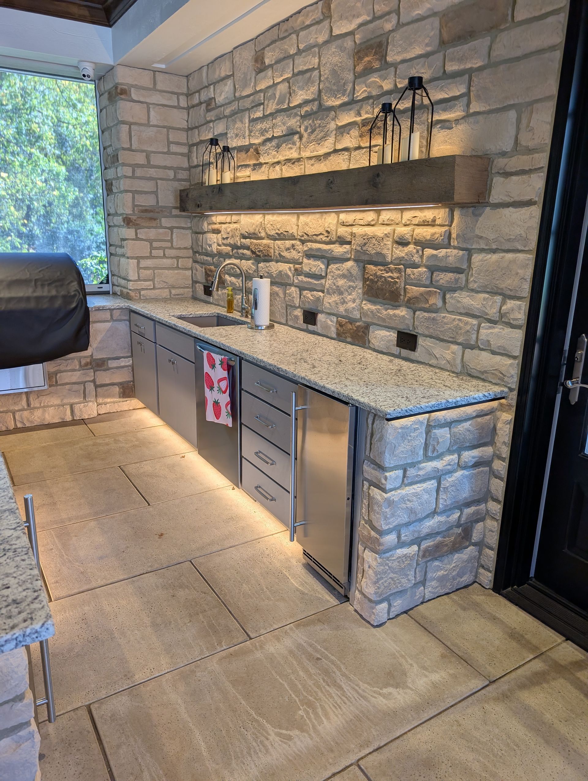 Outdoor kitchen with stone walls, stainless steel appliances, and granite countertop.
