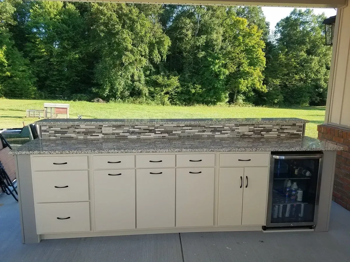 Outdoor kitchen with cream cabinets, granite countertop, tile backsplash, and mini fridge.