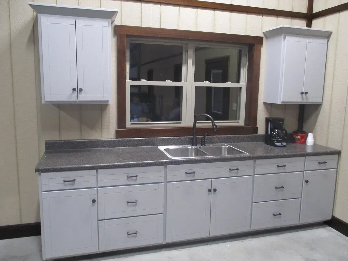 Kitchen cabinets with a sink and window, light blue cabinets, dark countertop, coffee maker.