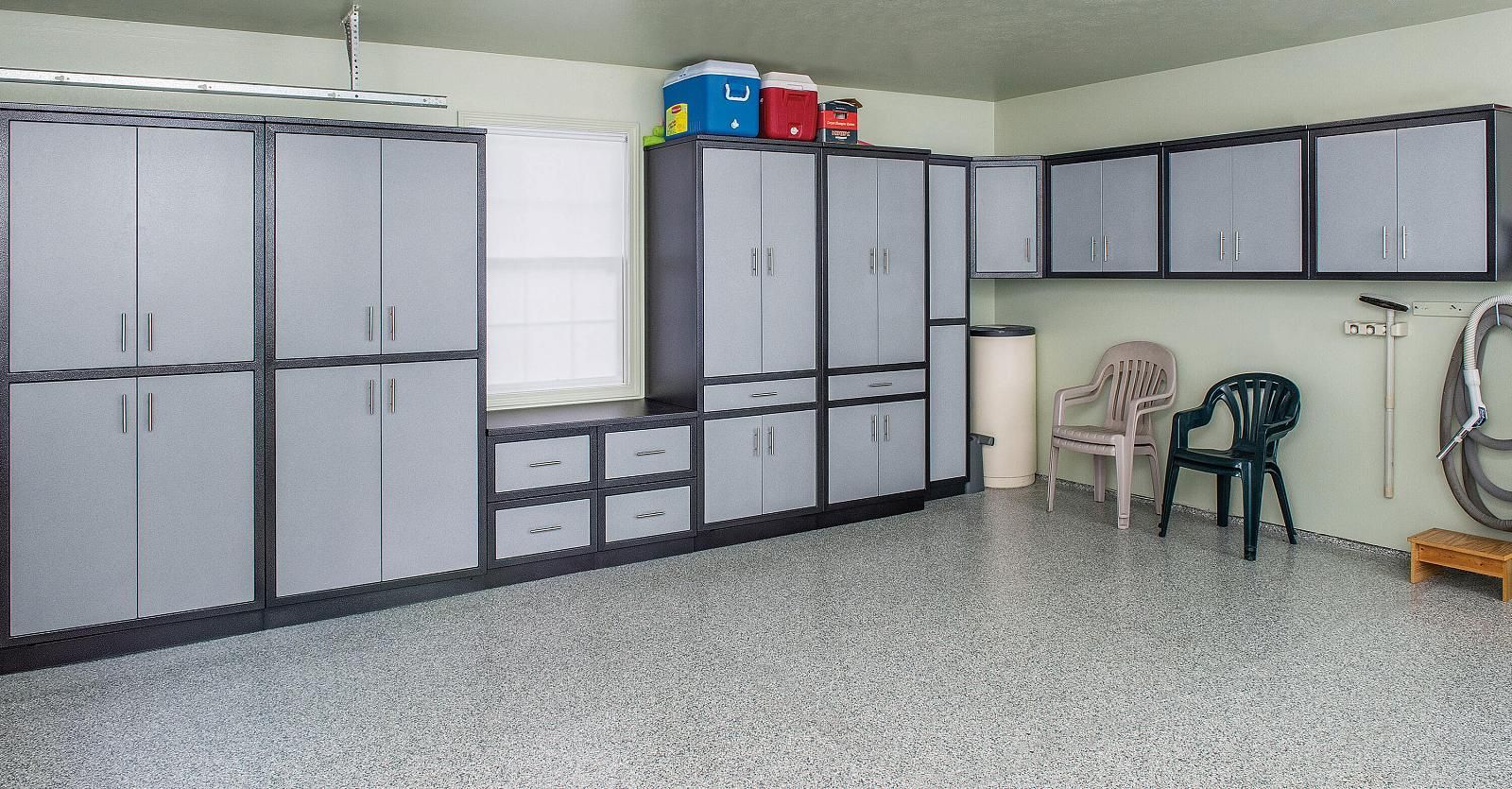 Garage interior with gray storage cabinets, a speckled floor, and two plastic chairs.