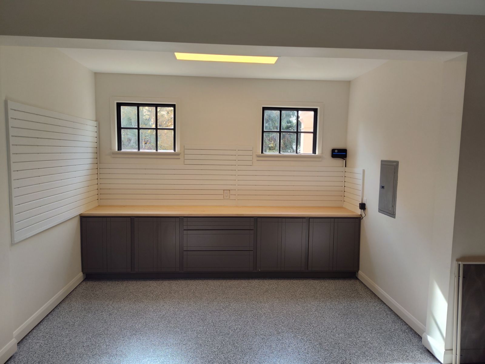 Garage interior with gray cabinets, wood countertop, two windows, and epoxy floor.