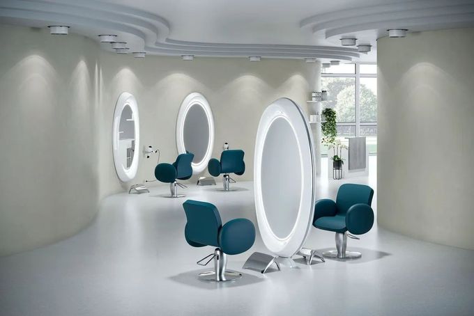 Un moderno interno da salone caratterizzato da specchi circolari retroilluminati e sedie color verde acqua disposte su un pavimento chiaro.