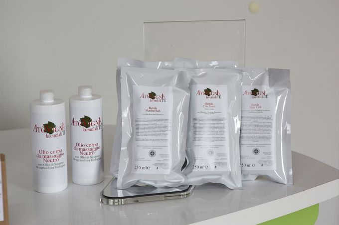 Una collezione di flaconi e vasetti di prodotti per la cura della pelle di marca, disposti su un bancone bianco, con uno sfondo che raffigura i loghi.