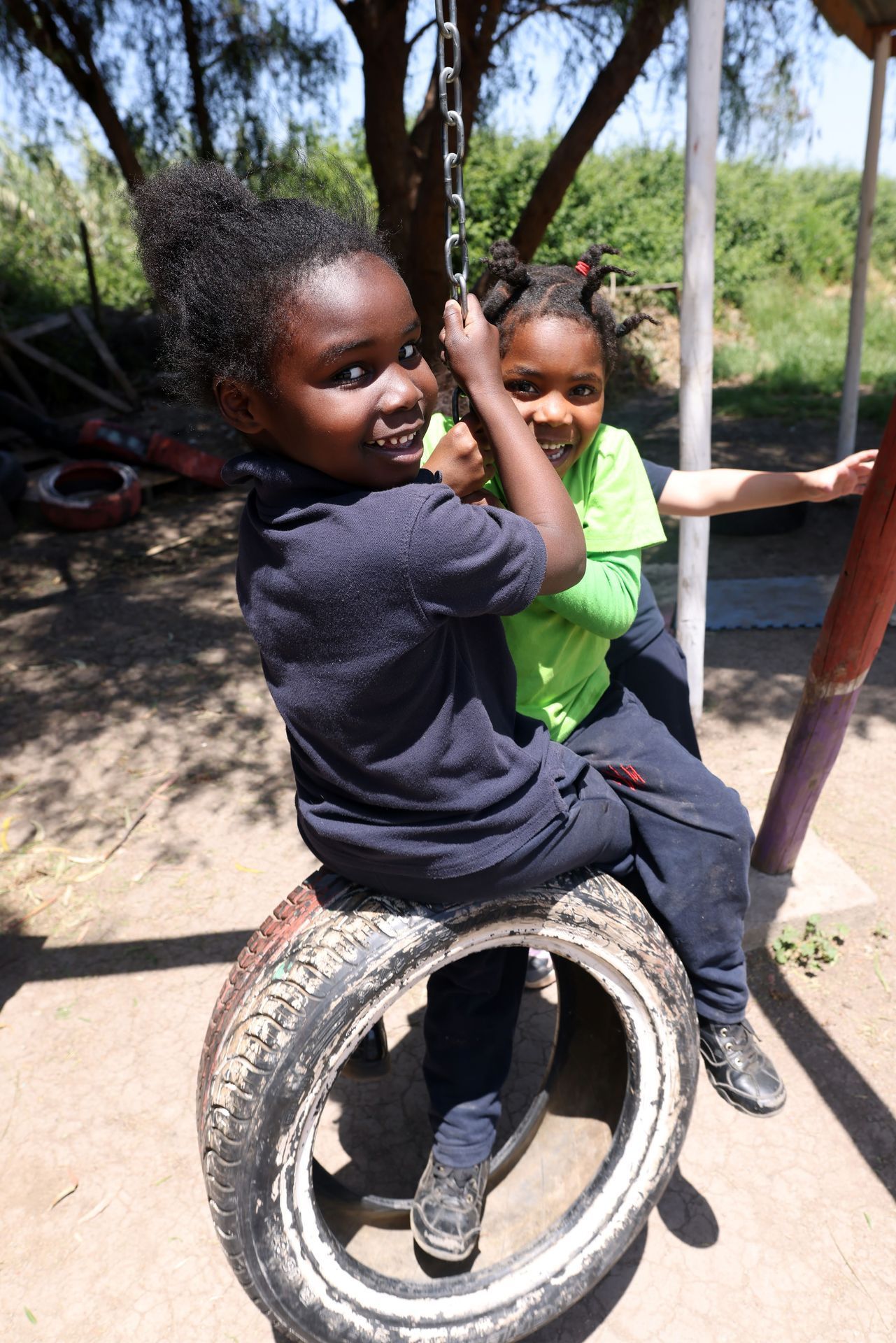 Dos niños en un columpio de neumático al aire libre, sonriendo. Uno sostiene la cadena.