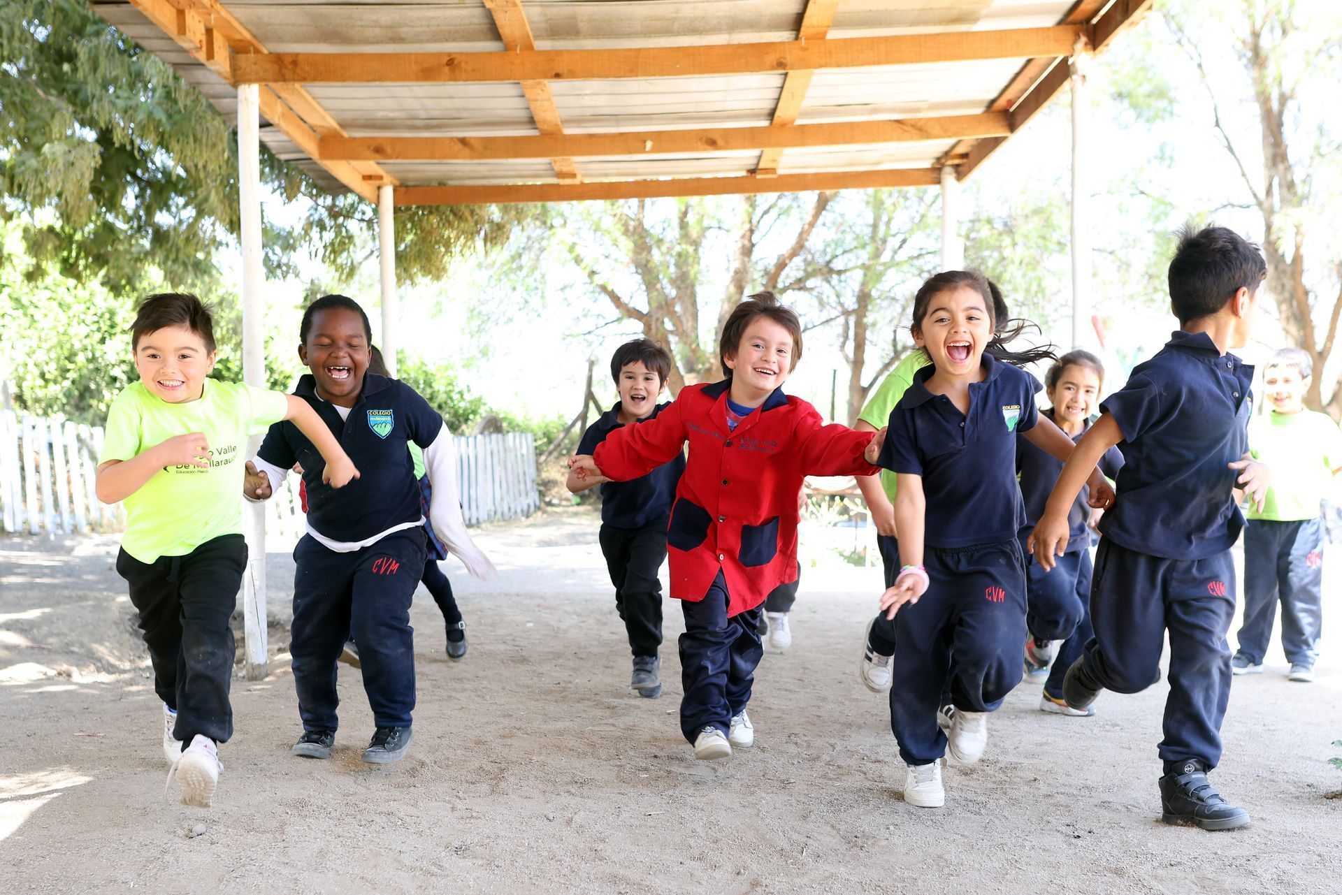 Niños corriendo alegremente al aire libre bajo un refugio de madera; día soleado.