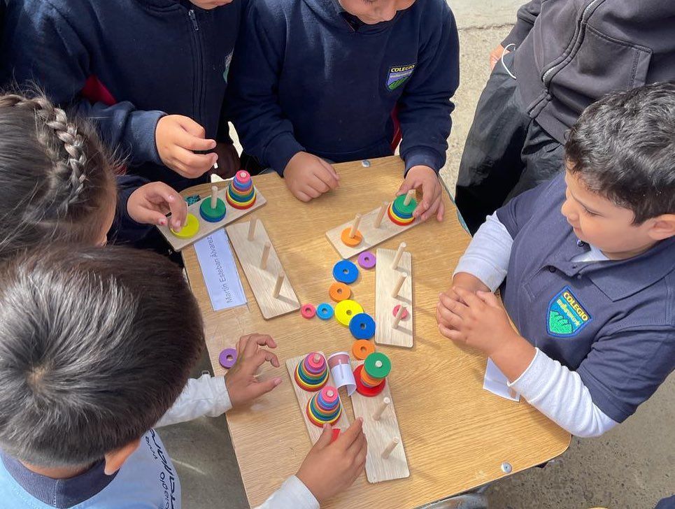 Niños jugando con juguetes de madera apilables en una mesa al aire libre.