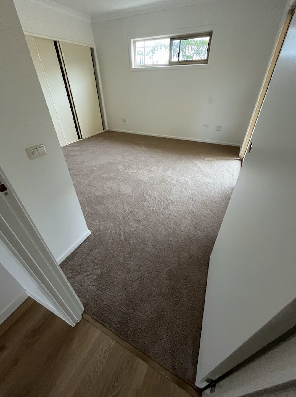 A Bedroom With Brown Carpet, White Walls, a Window, and a Sliding Door Closet — AGM Flooring & Tiling in Hidden Valley, QLD