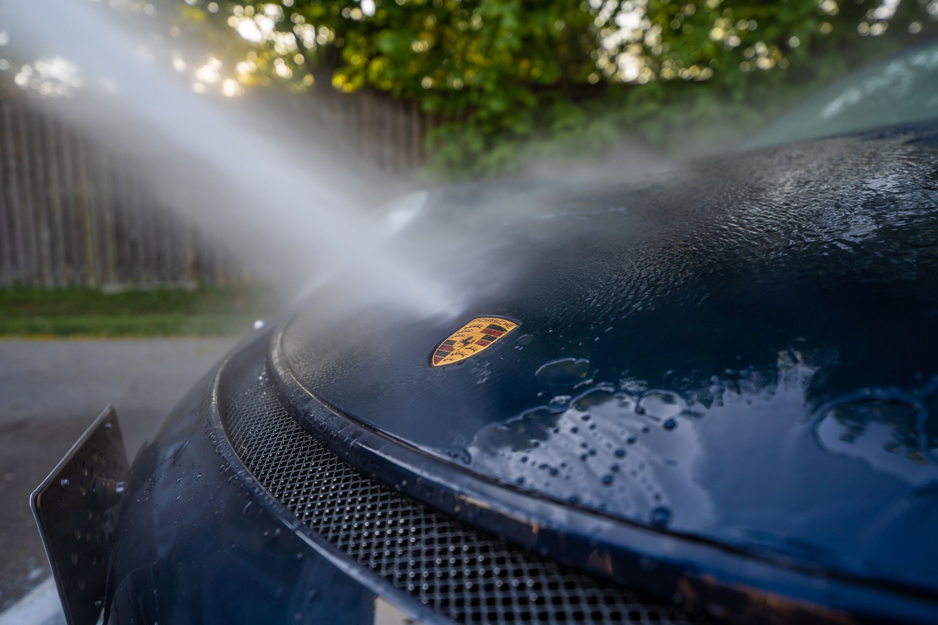 High-pressure water washing a dark blue car hood, with a rusty spot, outdoors.