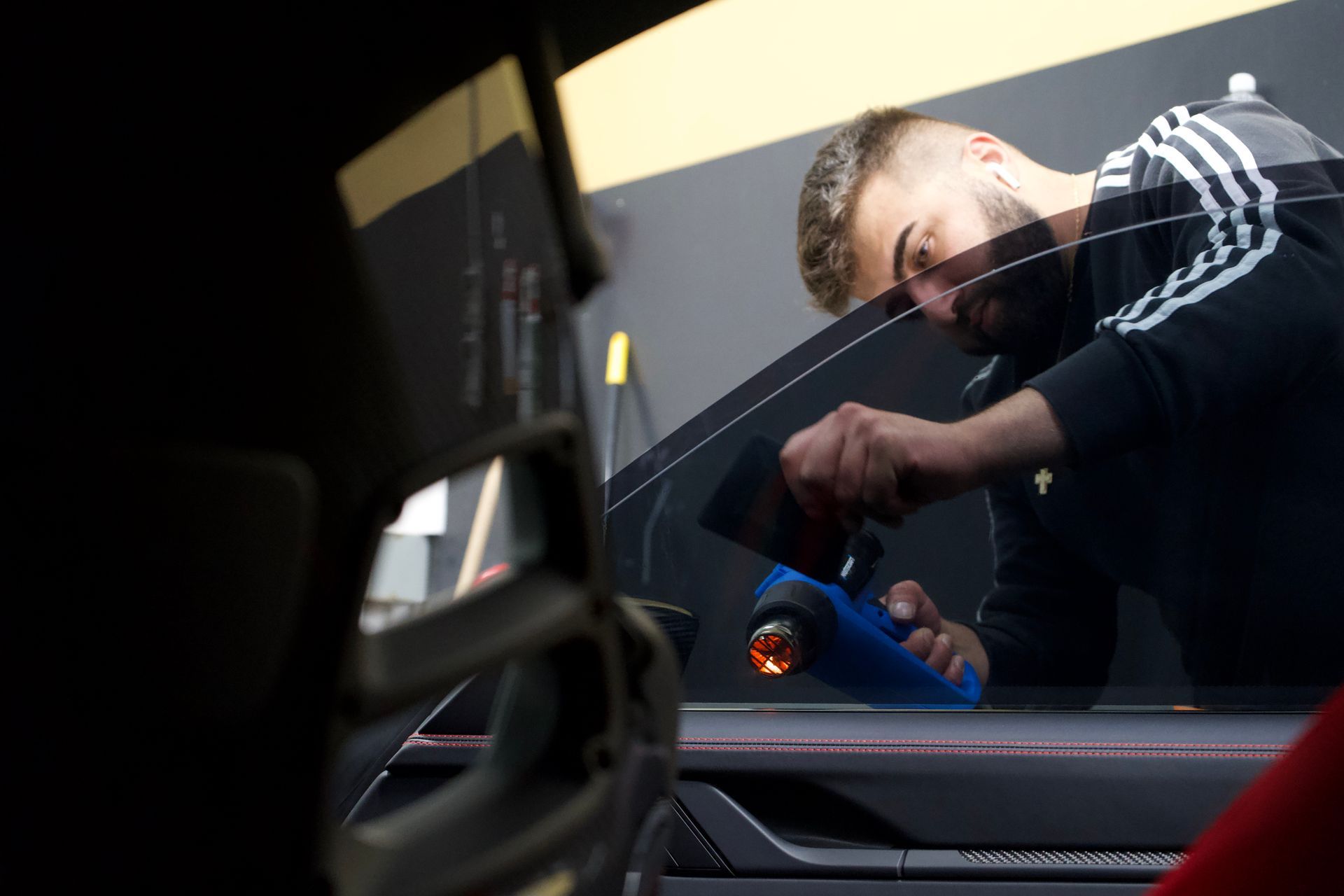 Man applying tint to a car window with a heat gun in a workshop.