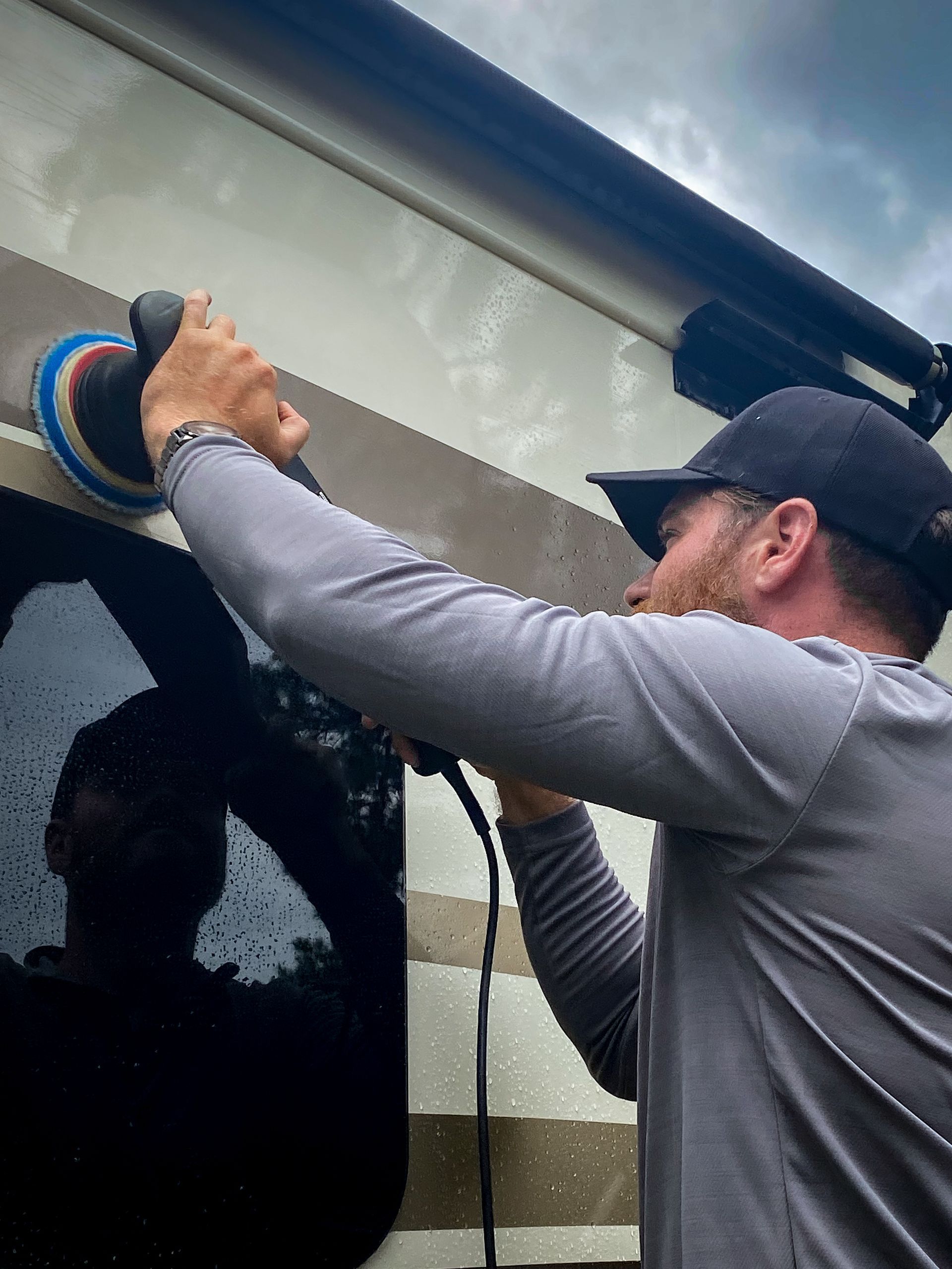 Worker washing a white van with a pressure washer outdoors in bright sunlight