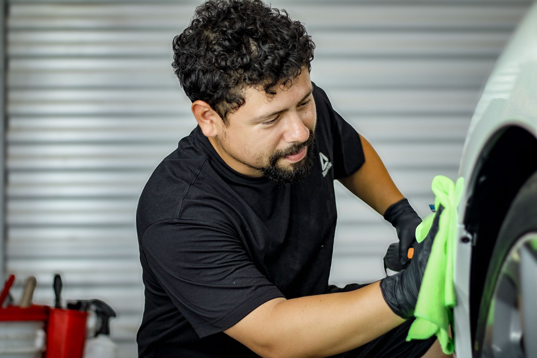 Gloved hand wiping the front bumper of a white car with a cloth