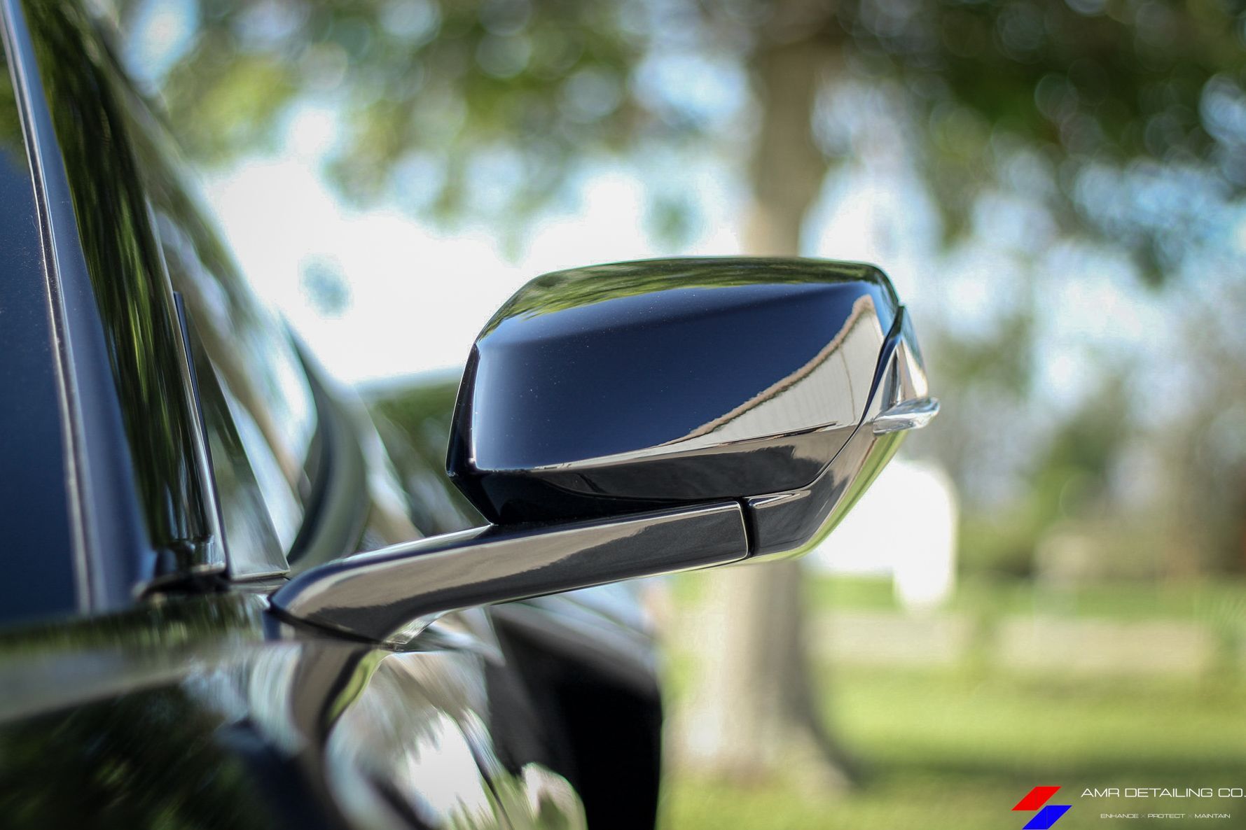 Close-up of a black car side mirror reflecting a sunny outdoor scene.