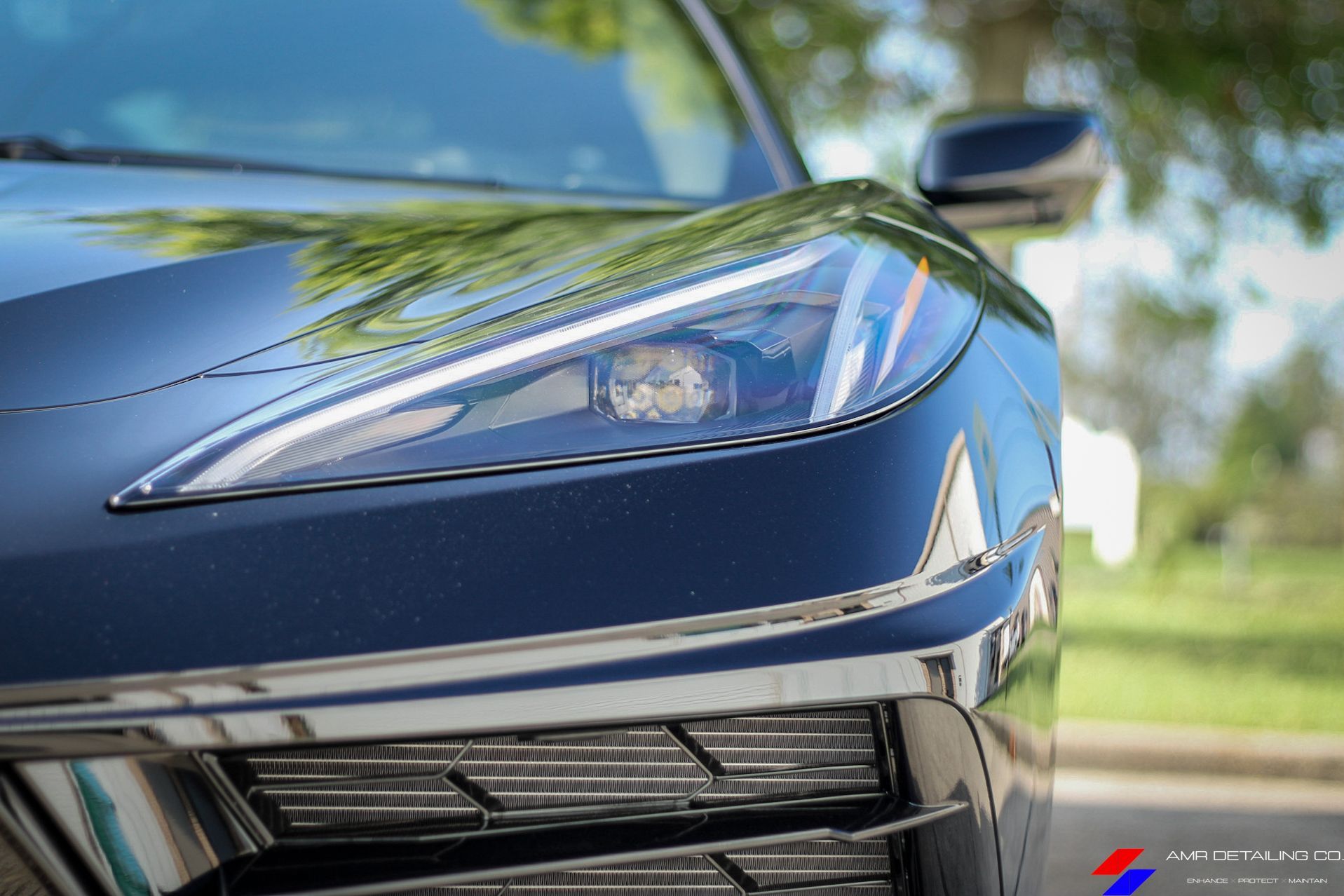 Close-up of a dark blue sports car’s front headlight and grille outdoors