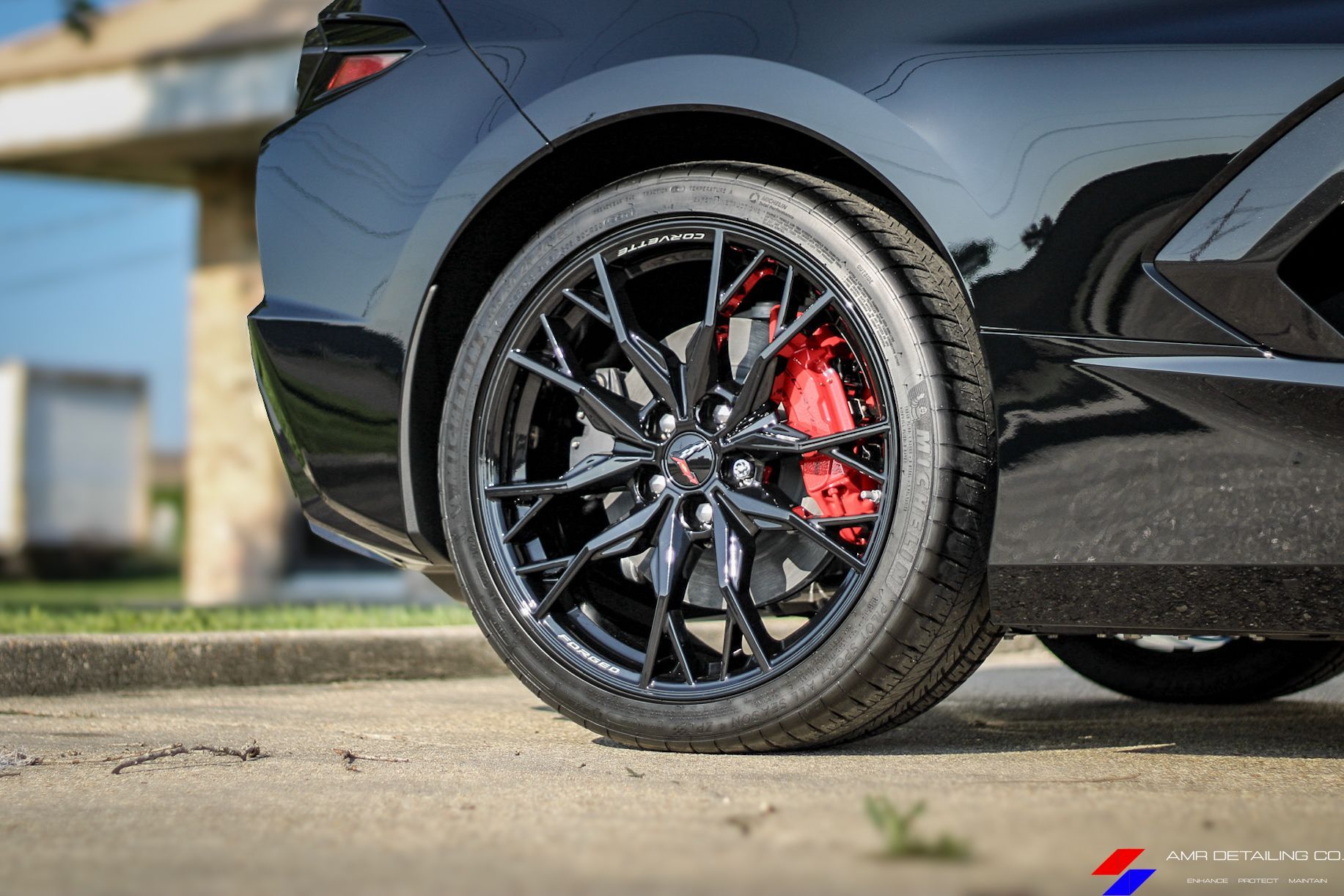 Black sports car rear wheel with red brake caliper and glossy body parked on pavement.
