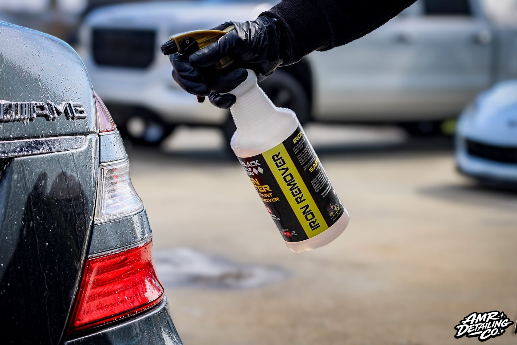 Person spraying a car’s rear quarter panel with a cleaning bottle at an auto wash site