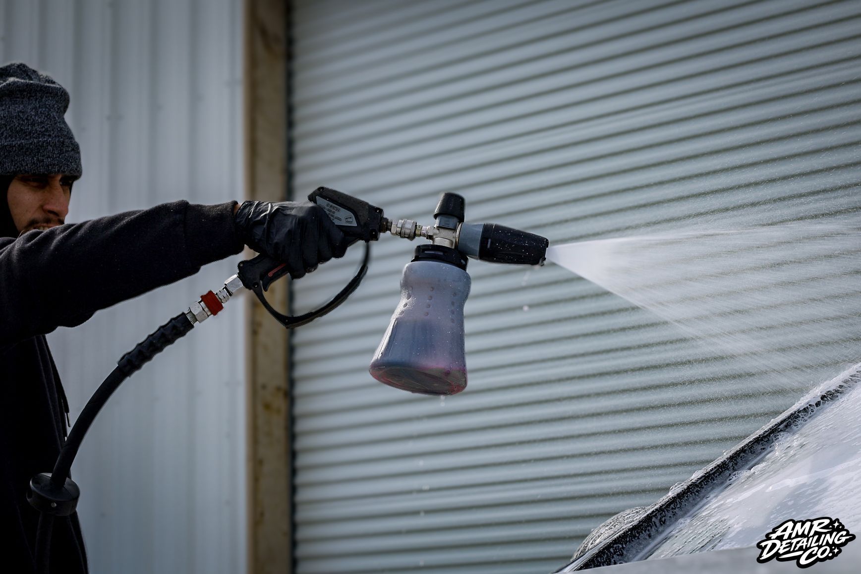 Person pressure-washing a car in front of a closed garage door.