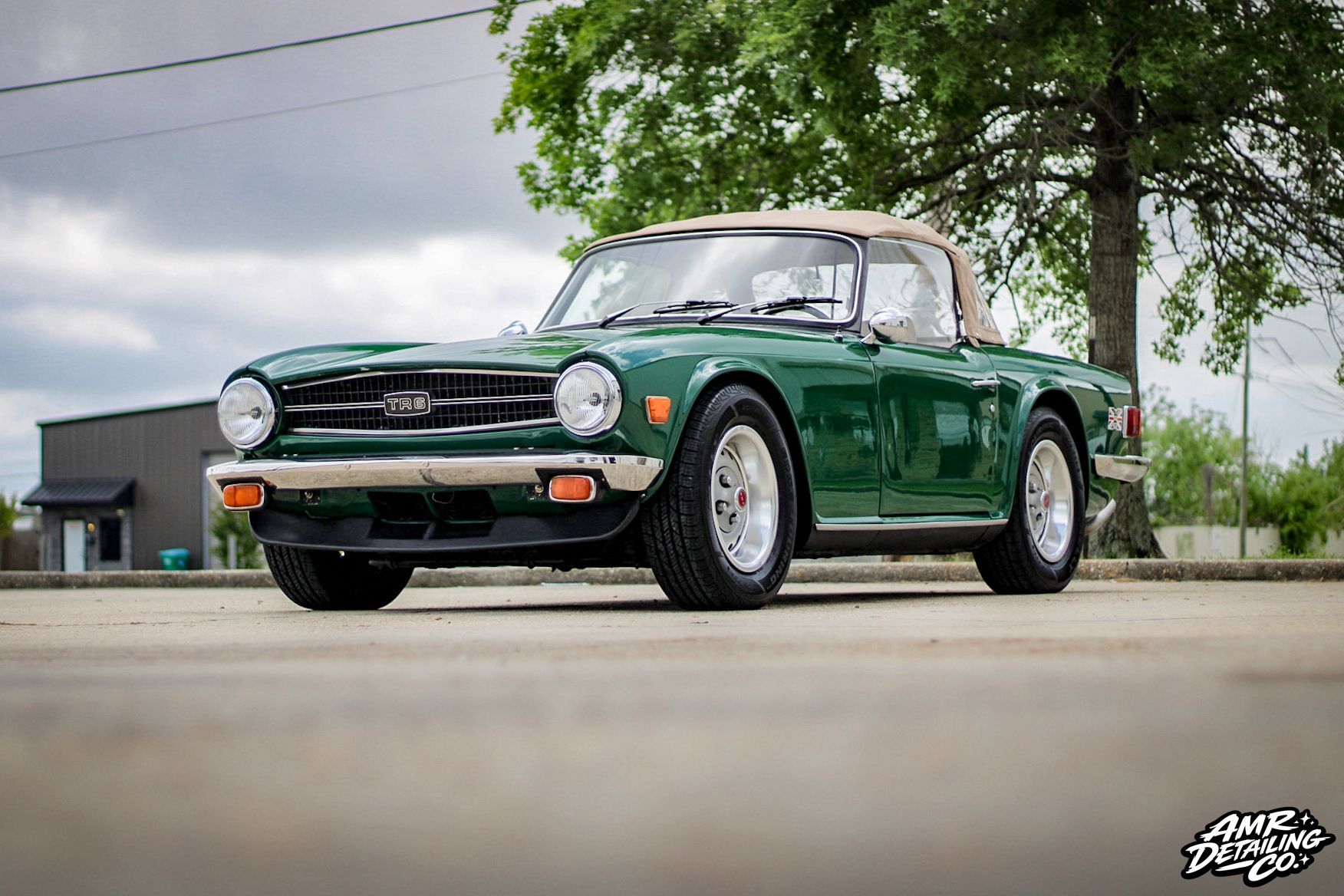 Green classic convertible car parked on a street under cloudy skies