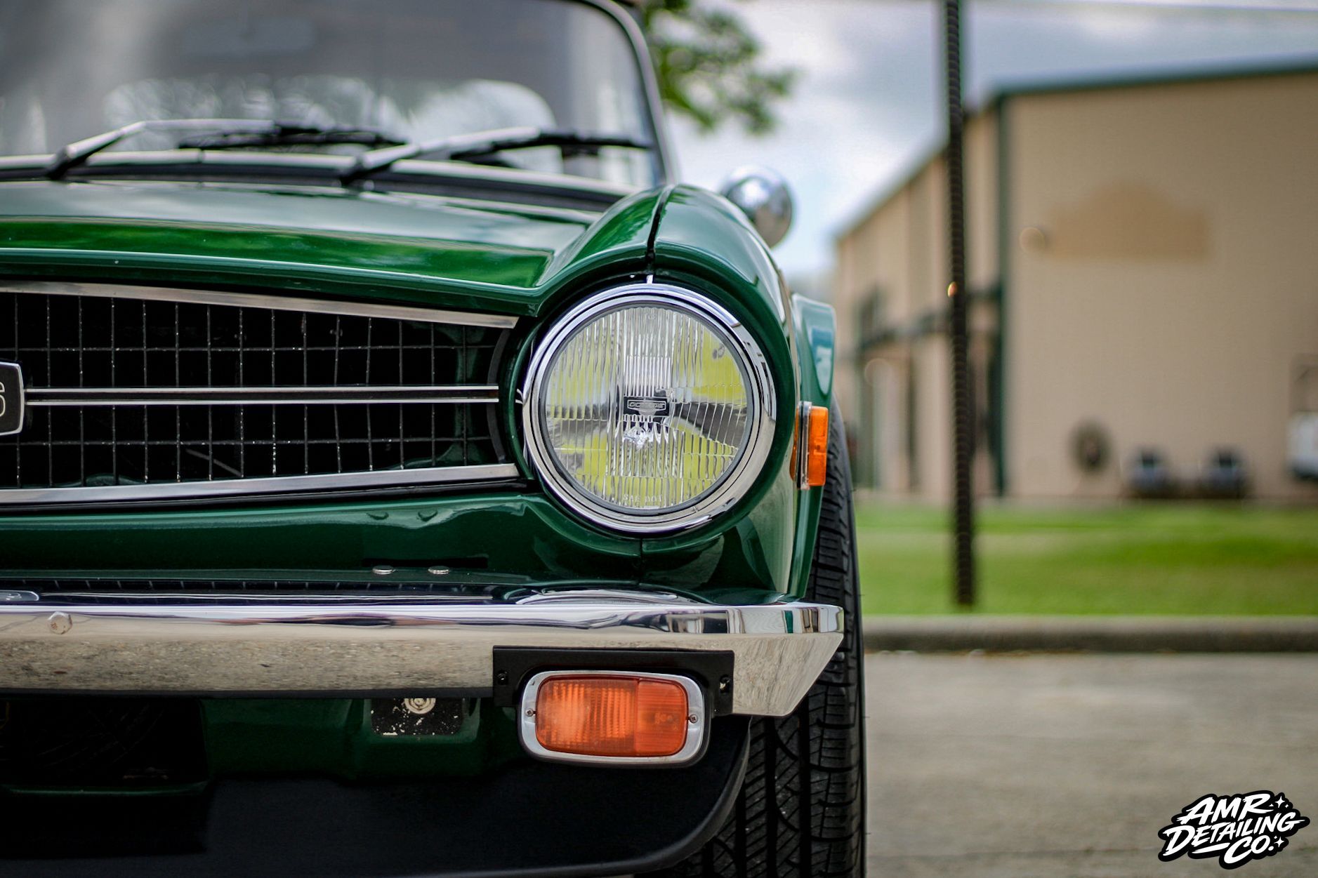 Front view of a dark green classic car with a chrome grille and round headlight