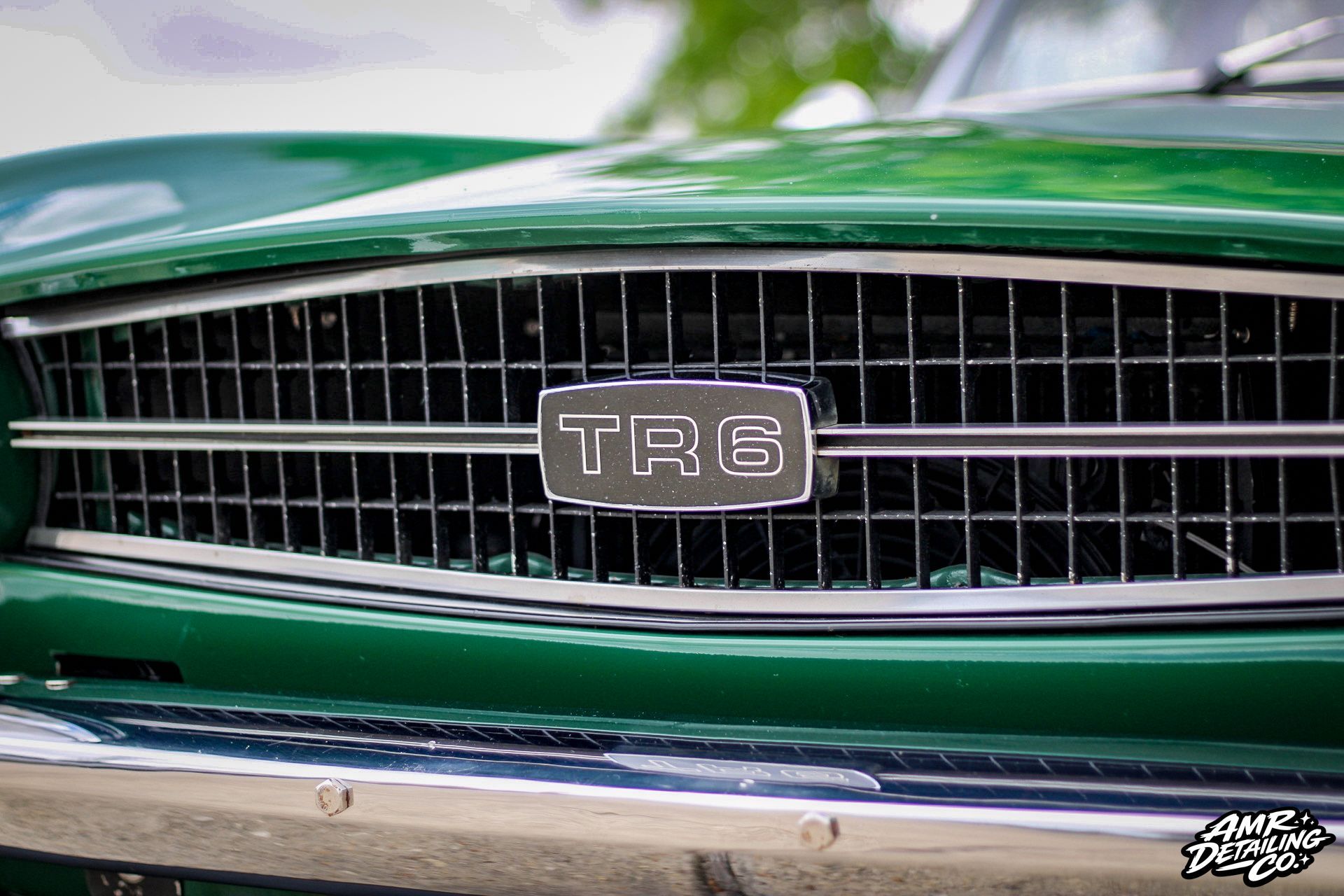 Close-up of a green classic car front grille with a TR6 badge and chrome bumper