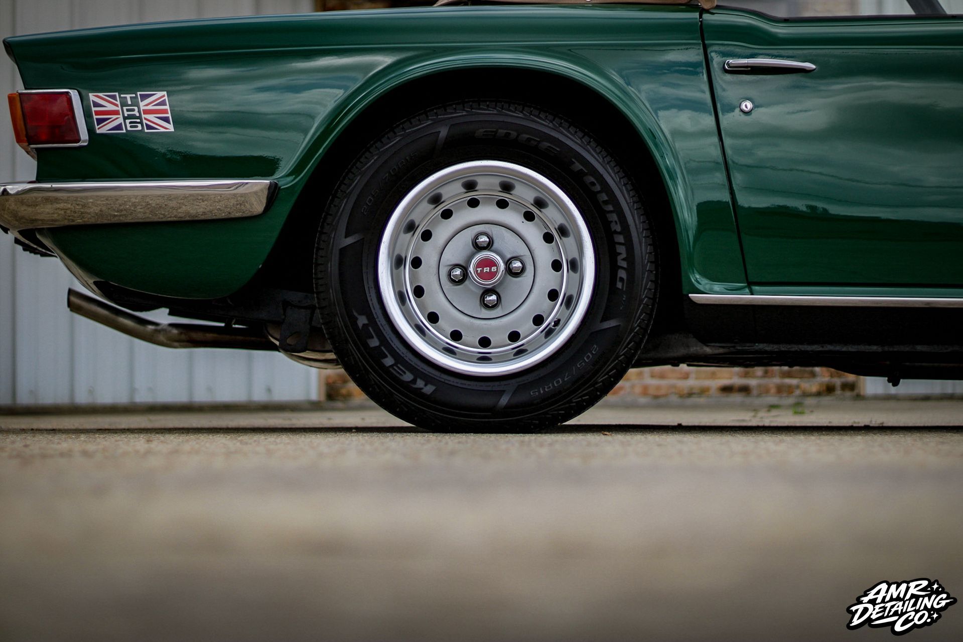 Close-up of a dark green classic car’s rear wheel and fender with chrome trim