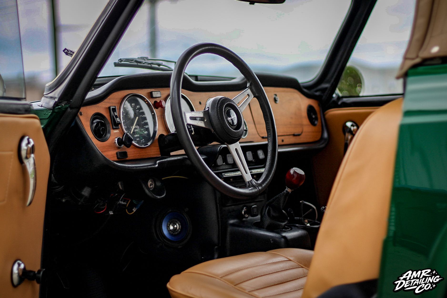 Classic car interior with tan leather seats, wood dashboard, and steering wheel exposed to the cabin.