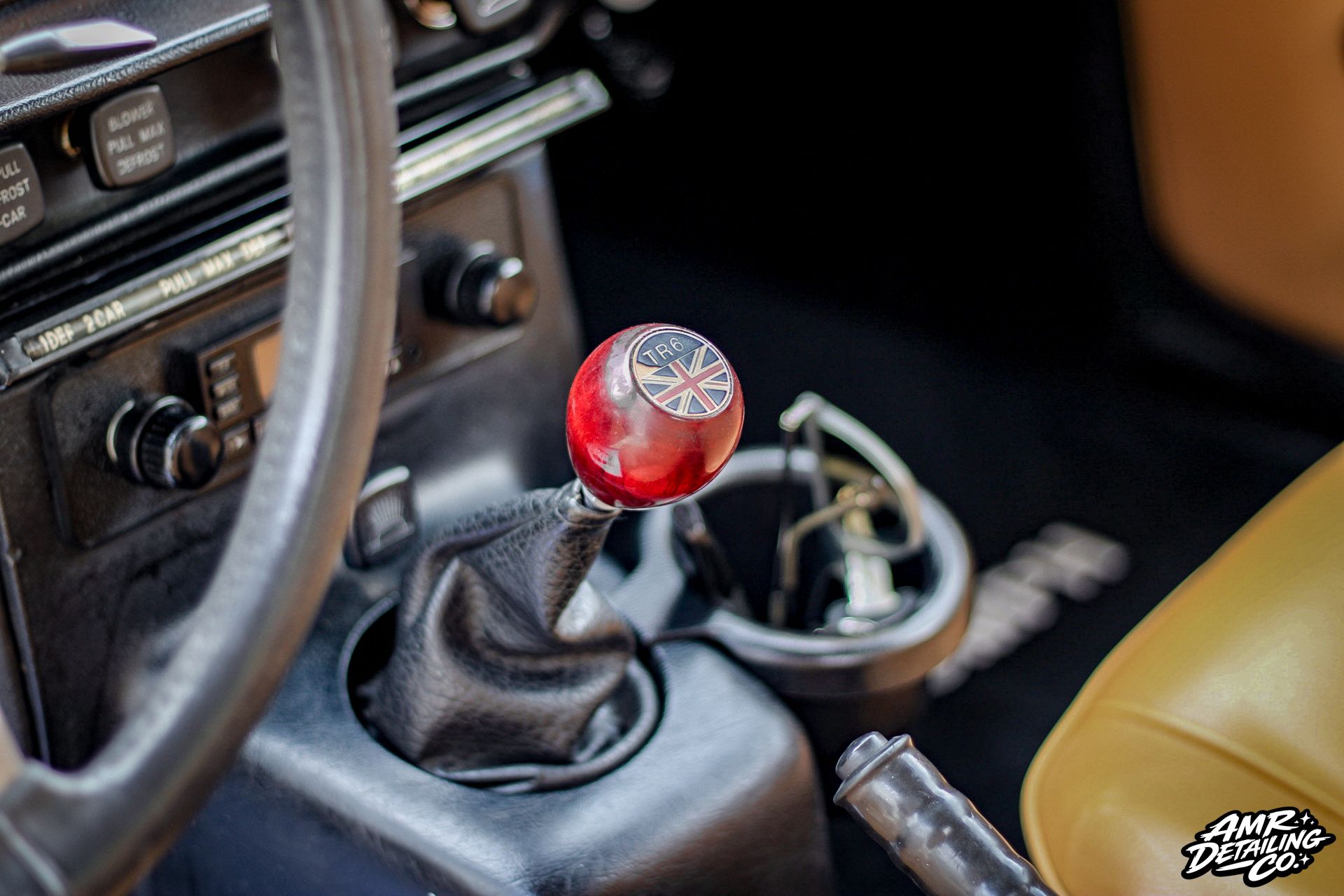 Classic car interior with steering wheel, red manual gear shift knob, and tan seat