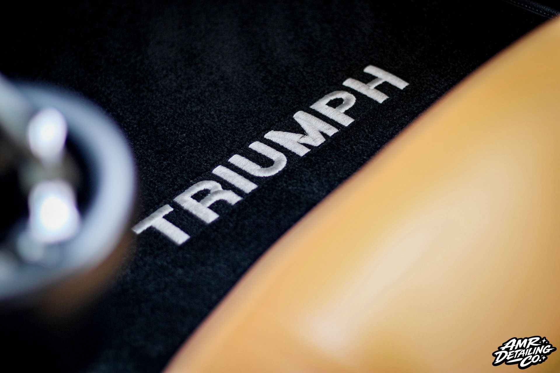 Close-up of a Triumph logo on a black motorcycle tank with gold bodywork