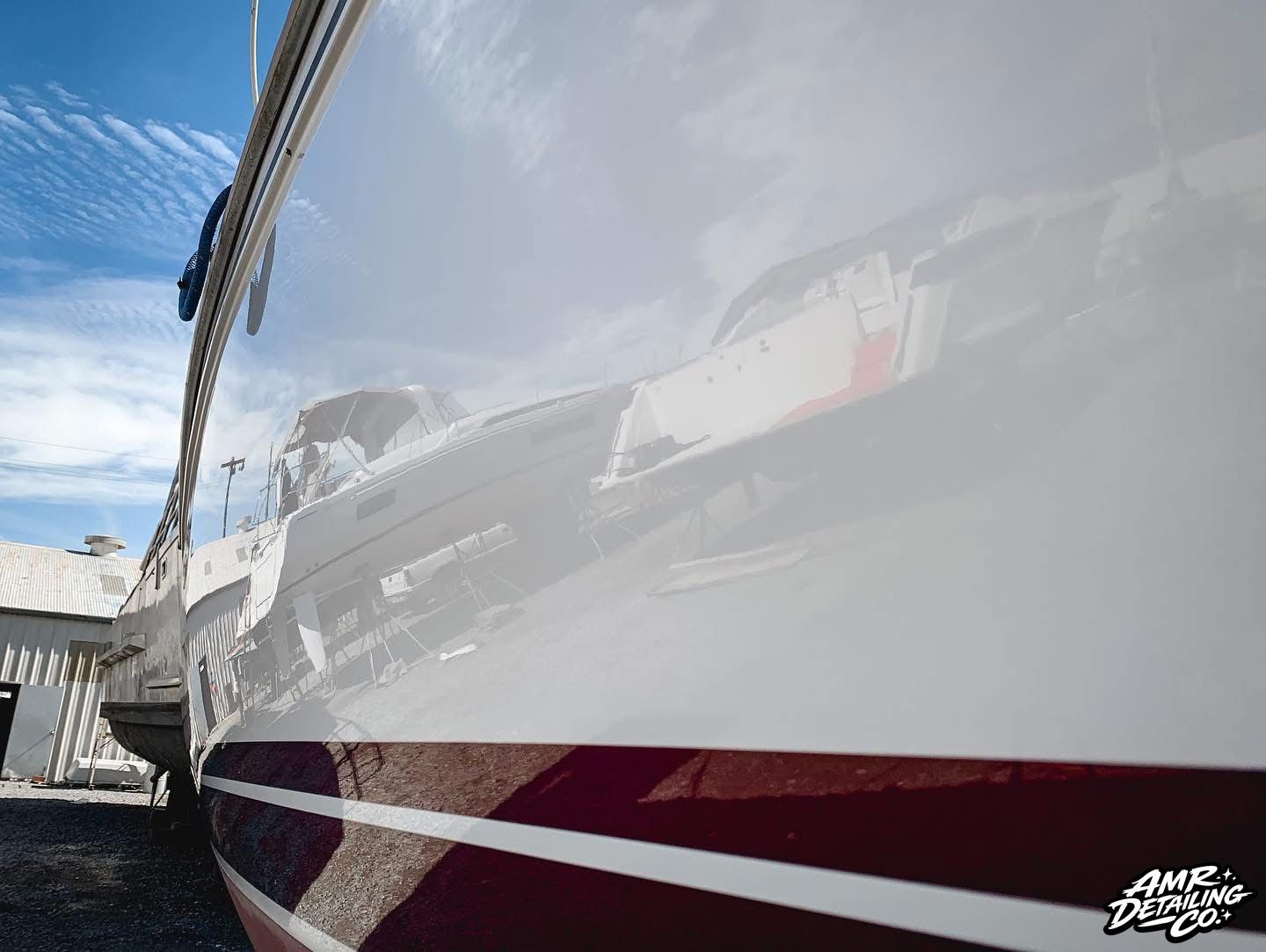 Close-up of a white boat hull with maroon stripe, reflecting the sky at a marina