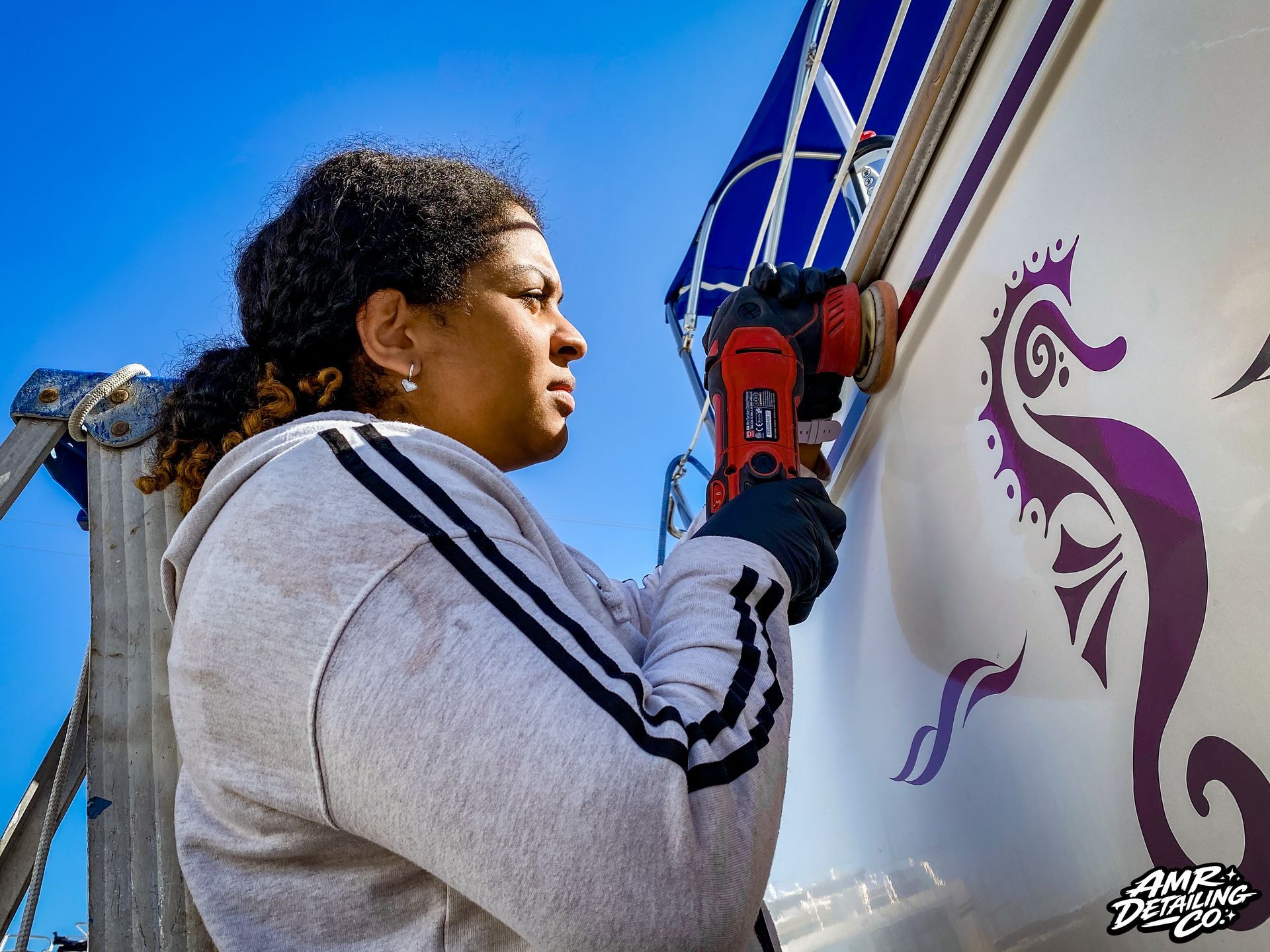 Person spray-painting a white wall with a purple mural under a blue sky