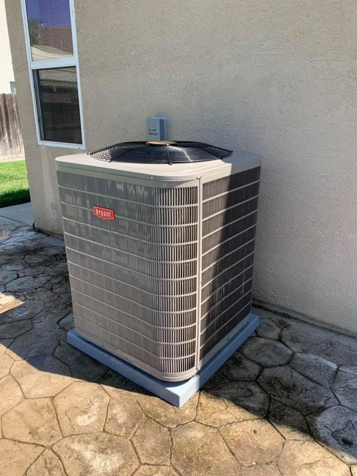 Bryant outdoor condenser unit installed on stamped concrete patio near a window.