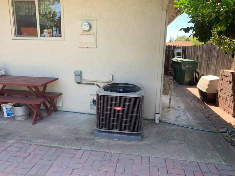 Bryant air conditioner unit installed on a concrete pad next to a picnic table in a backyard.