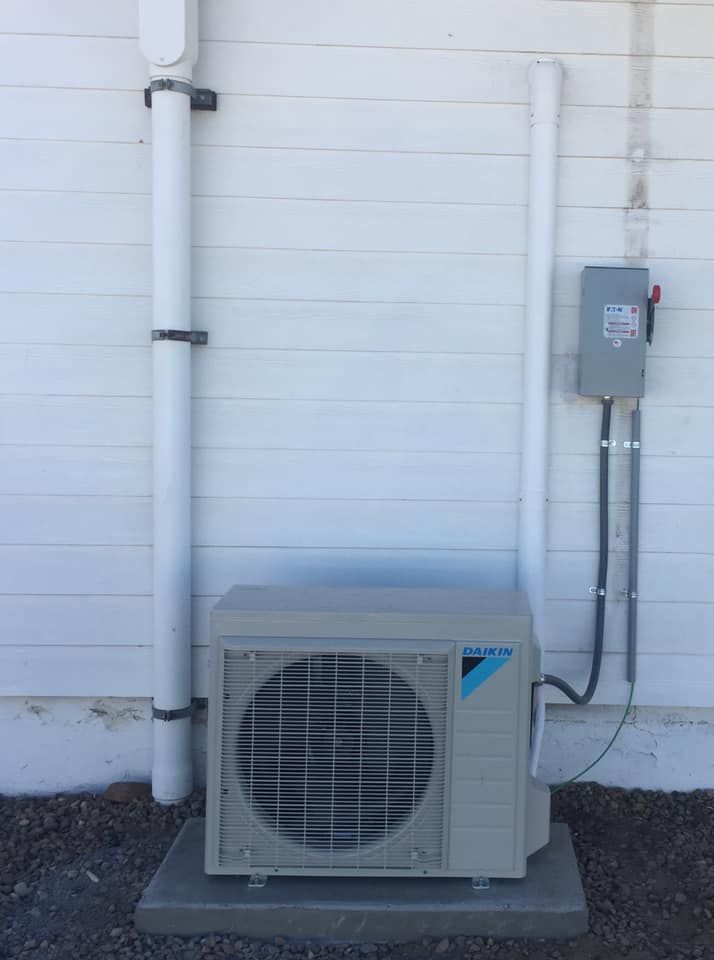 Daikin mini split condenser mounted on white wall.
