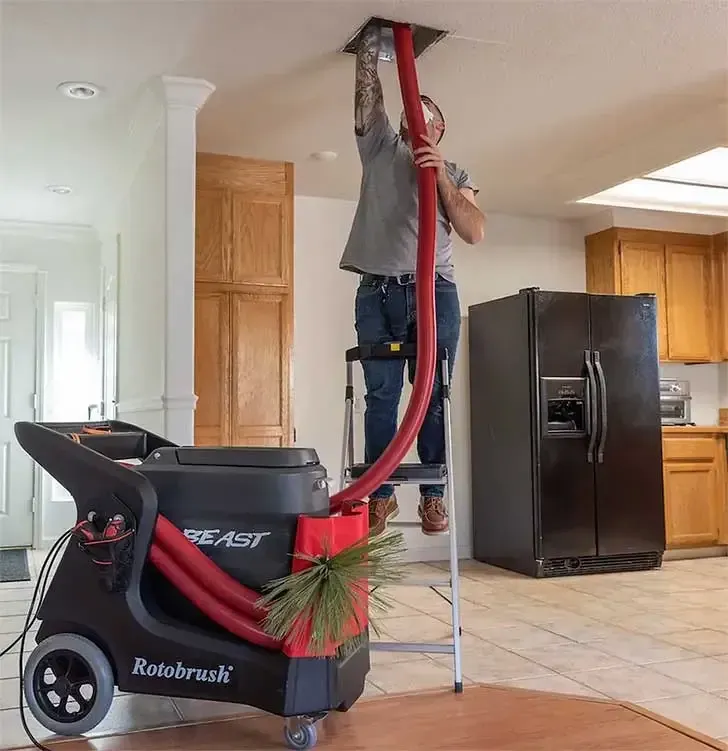 Technician using Rotobrush system to clean ceiling air duct in a residential kitchen.