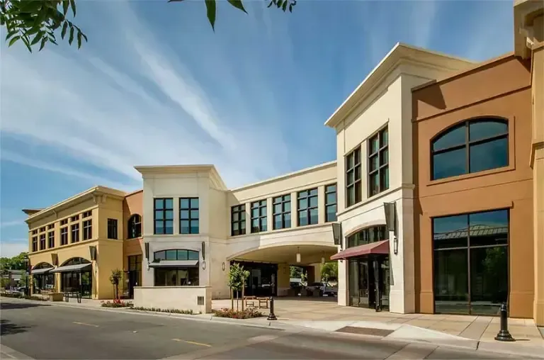 A large building with a lot of windows is surrounded by smaller buildings.