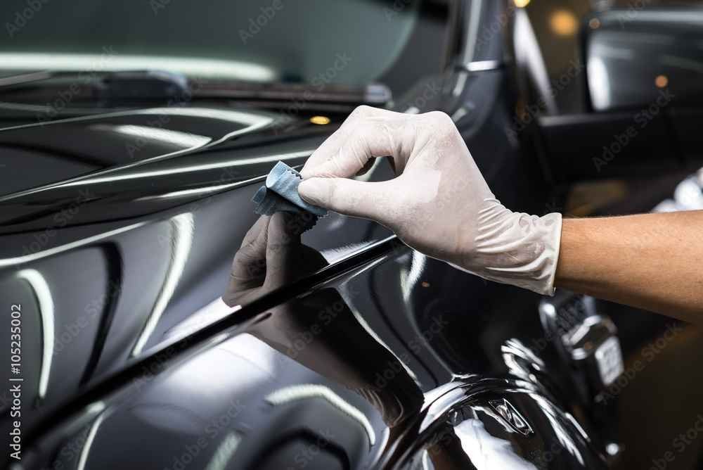 Gloved hand polishing a black car’s glossy surface with a cloth
