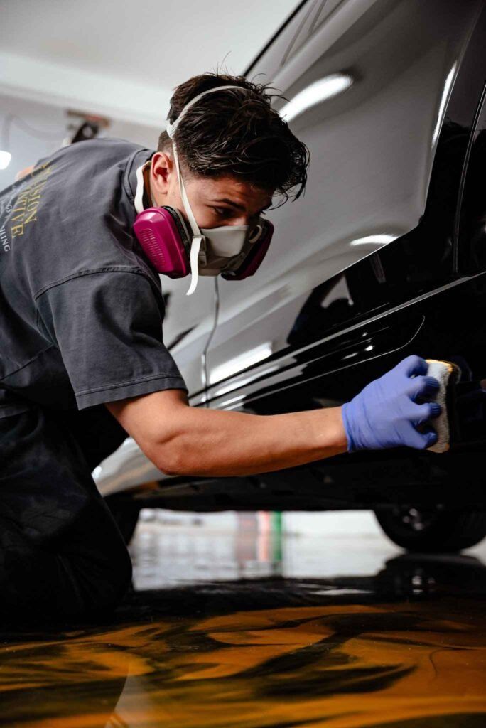 Mechanic wearing gloves and respirator polishing a black car in a garage