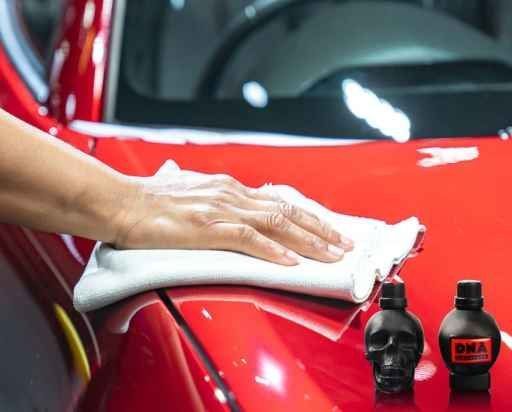 Hand polishing a red car with a white cloth beside detailing bottles