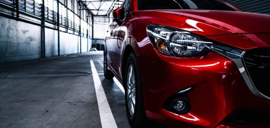 Red car parked in a dim industrial garage, showing its front headlight and grille close-up