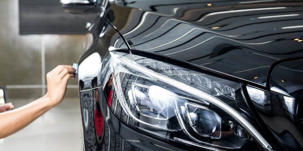 Hand polishing the front of a black car near the headlight in a garage