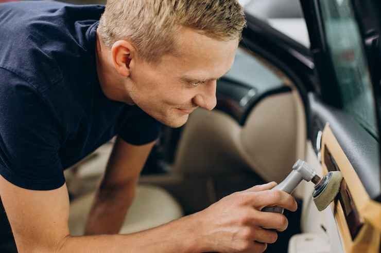 Man polishing a car interior door panel with a handheld tool