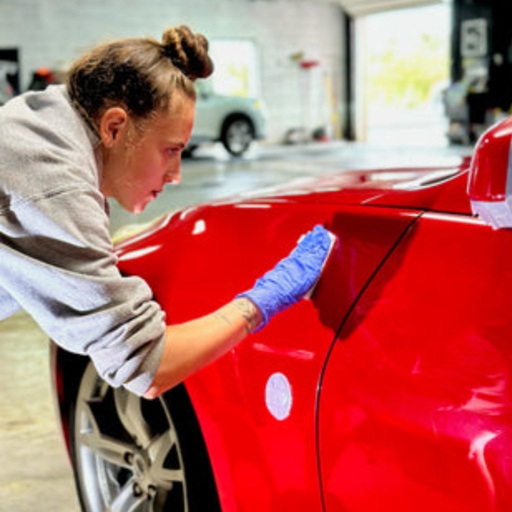 Person cleaning a red sports car with a cloth and gloves in a garage