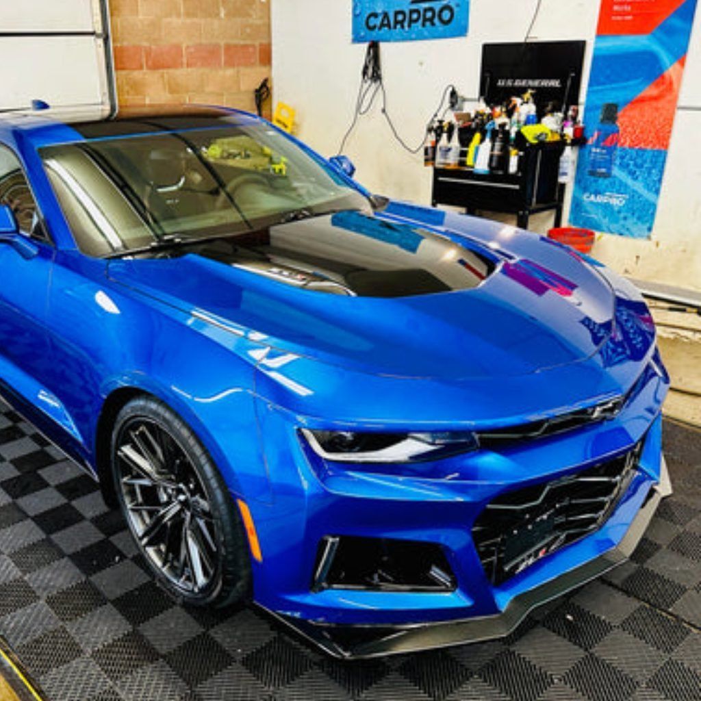Blue sports car parked indoors on a checkered floor in a car detailing shop