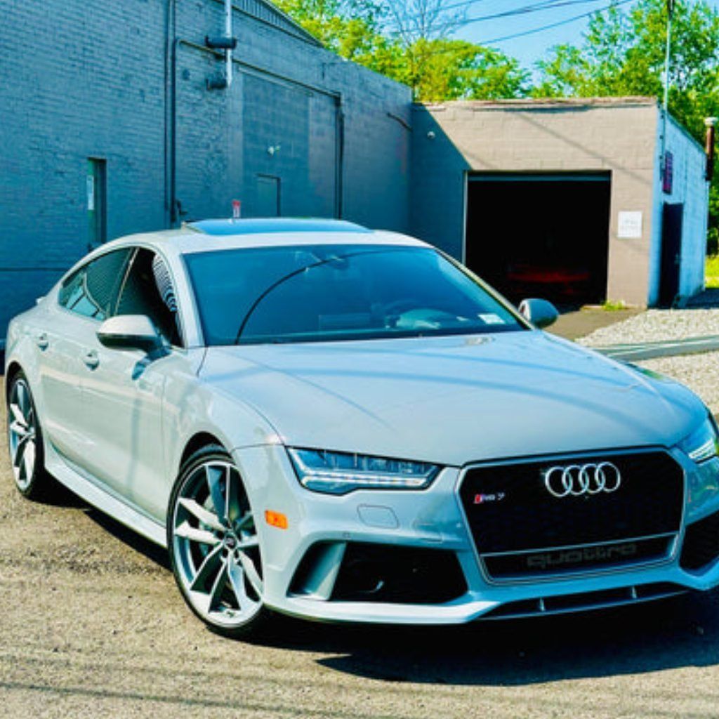 White Audi sedan parked in an alley beside a brick building, front three-quarter view.