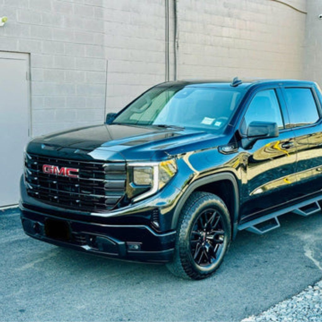 Black GMC pickup truck parked beside a building on a sunny street.