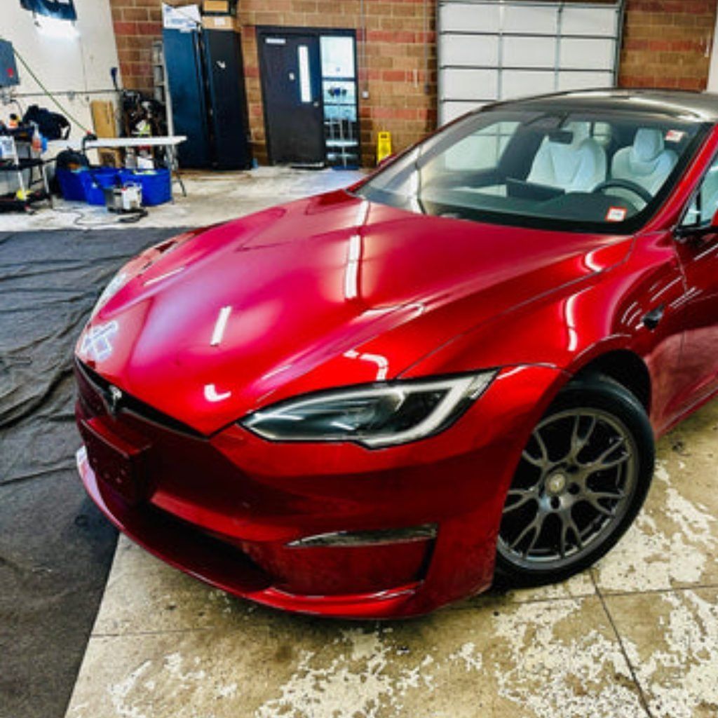 Red Tesla parked in a garage, with a glossy finish and front-left view.