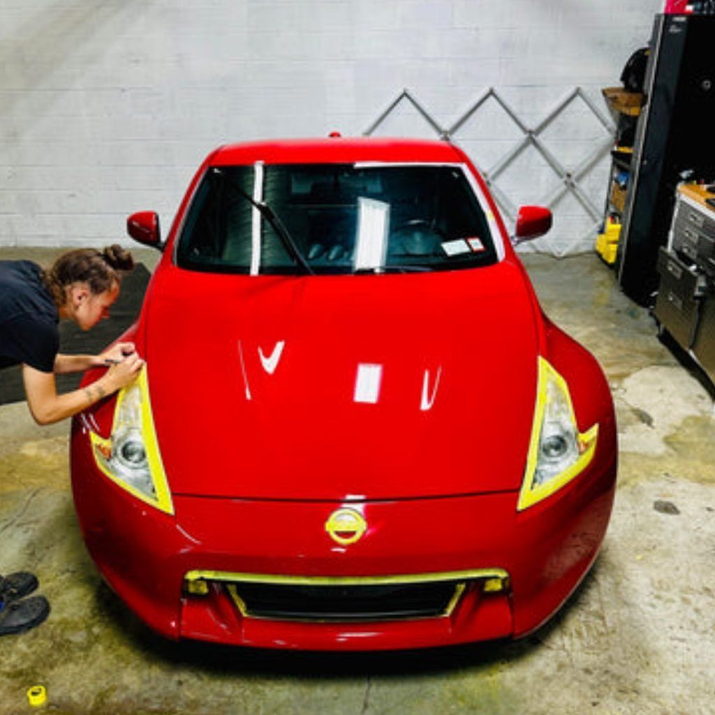 Red sports car being detailed in a garage, with a person polishing the front left headlight.