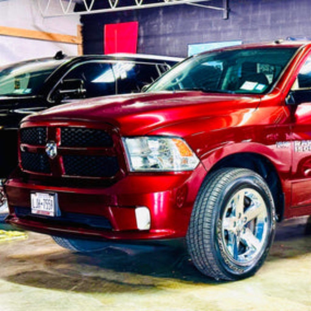 Red Dodge pickup truck displayed indoors, front three-quarter view with chrome wheels and a black vehicle behind it